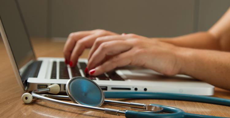 Photo of doctor at desk, hands seen on laptop