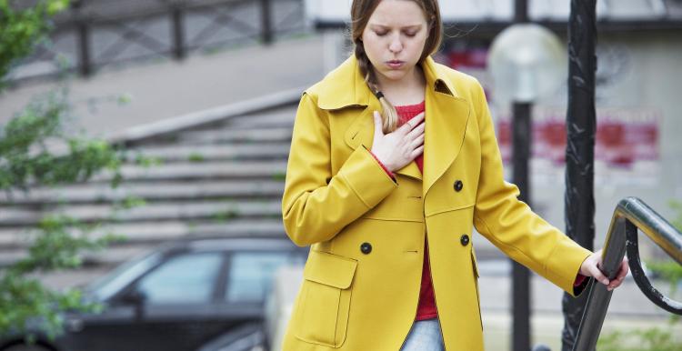 Young woman in yellow coat holding her chest in pain