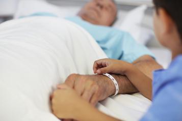 Nurse holding hands with an elderly patient lying in a hospital bed