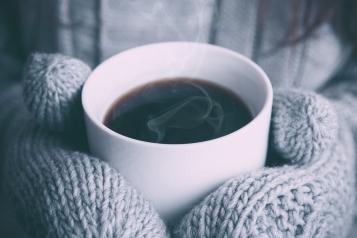 Person holding a hot cup of coffee wearing woolly gloves