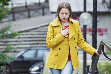 Young woman in yellow coat holding her chest in pain