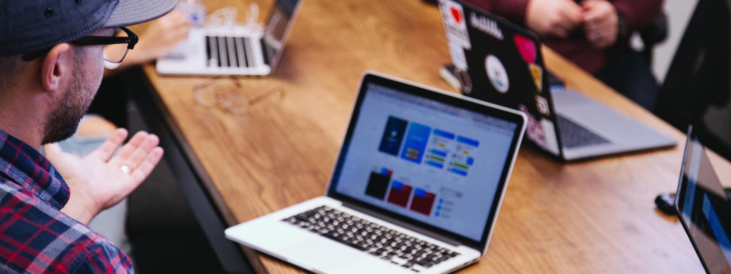 Photo of men at open laptops, faces not seen, in discussion