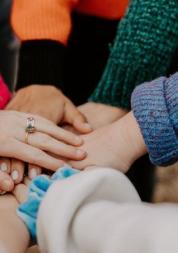 Photo of a circle of people with their hands joined in the middle of the circle 